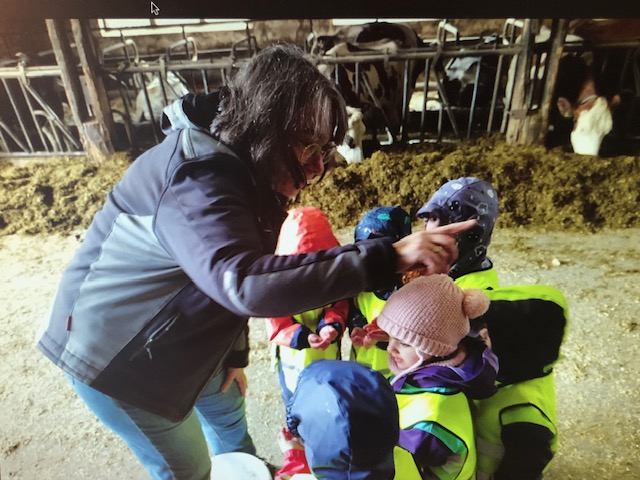 Eine Frau erklärt den Kindergartenkindern etwas im Kuhstall