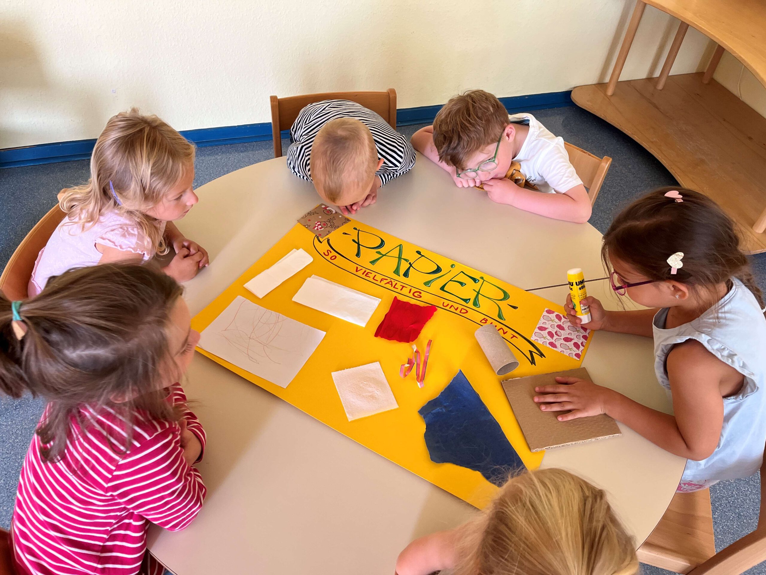 Kinder gestalten ein Plakat mit Papierbeispielen.