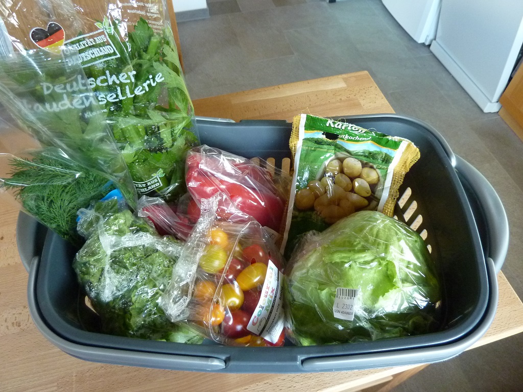 Ein Einkaufskorb voll mit in Plastik verpackten Obst und Gemüse.