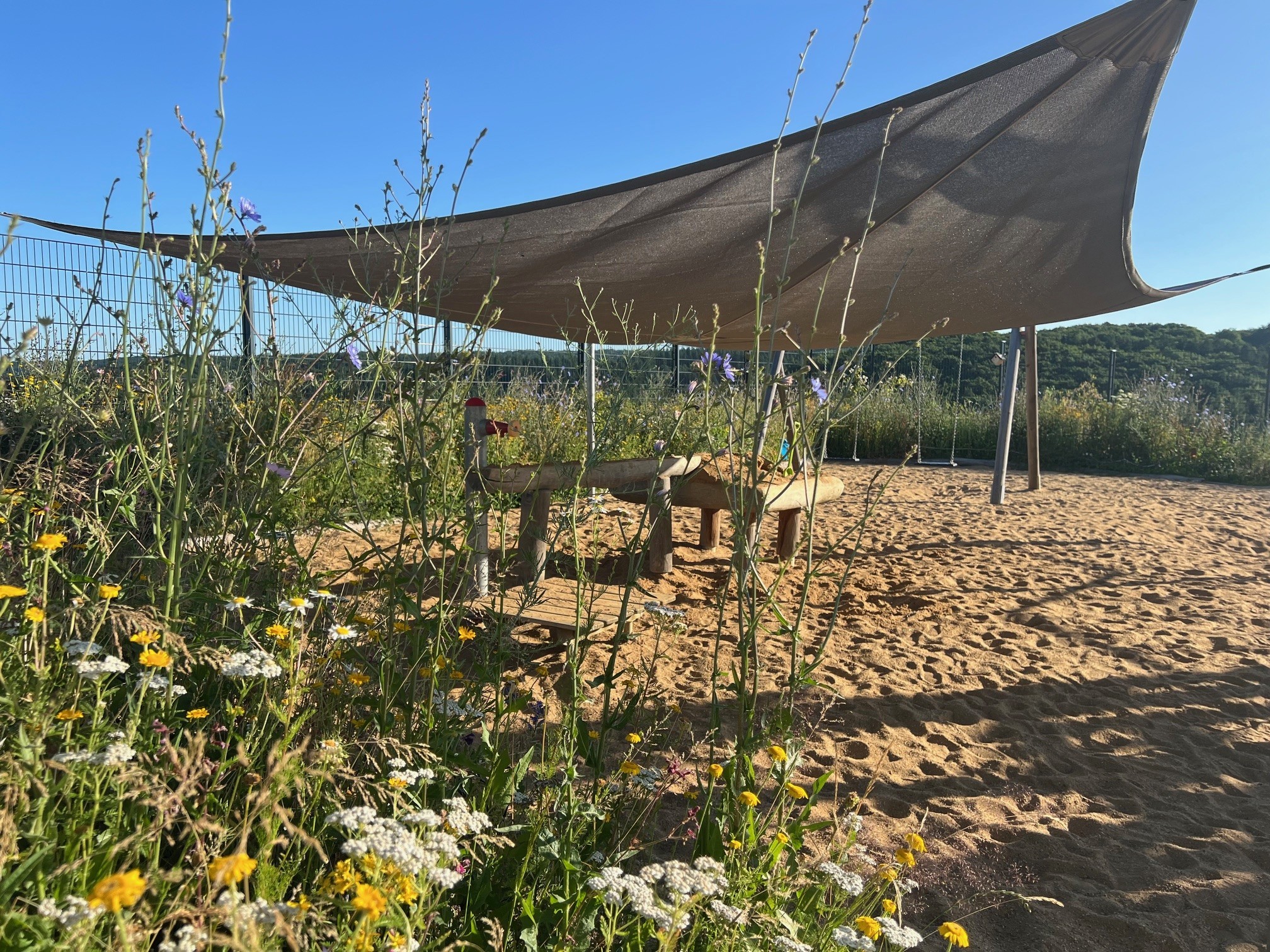 Ein Sandspielplatz mit Sonnensegel auf dem Kita-Außengelände.