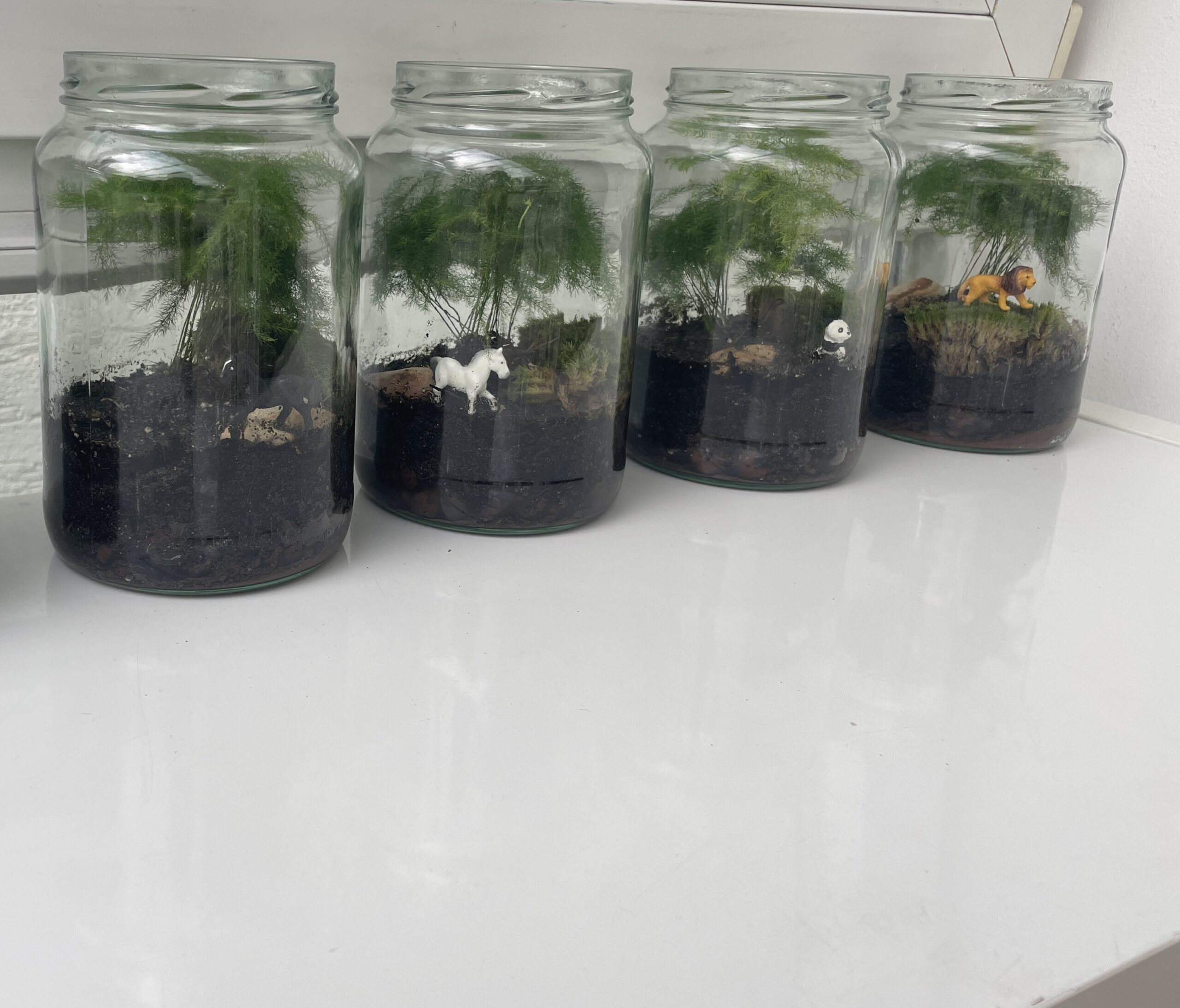 Glasflaschen mit Moos und Pflanzen sowie Tieren aus Plastik