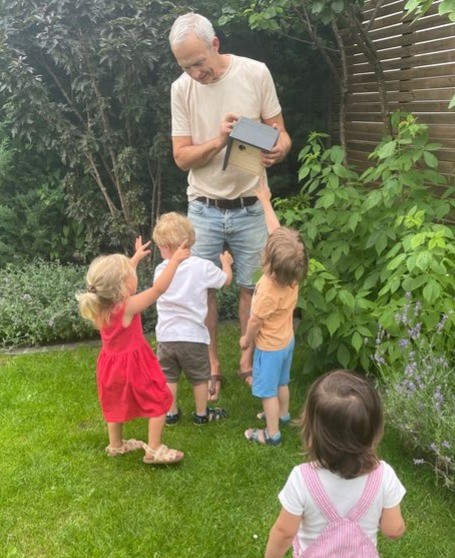 Kinder umringen einen Mann, der ein Vogelhaus aufhängen will.