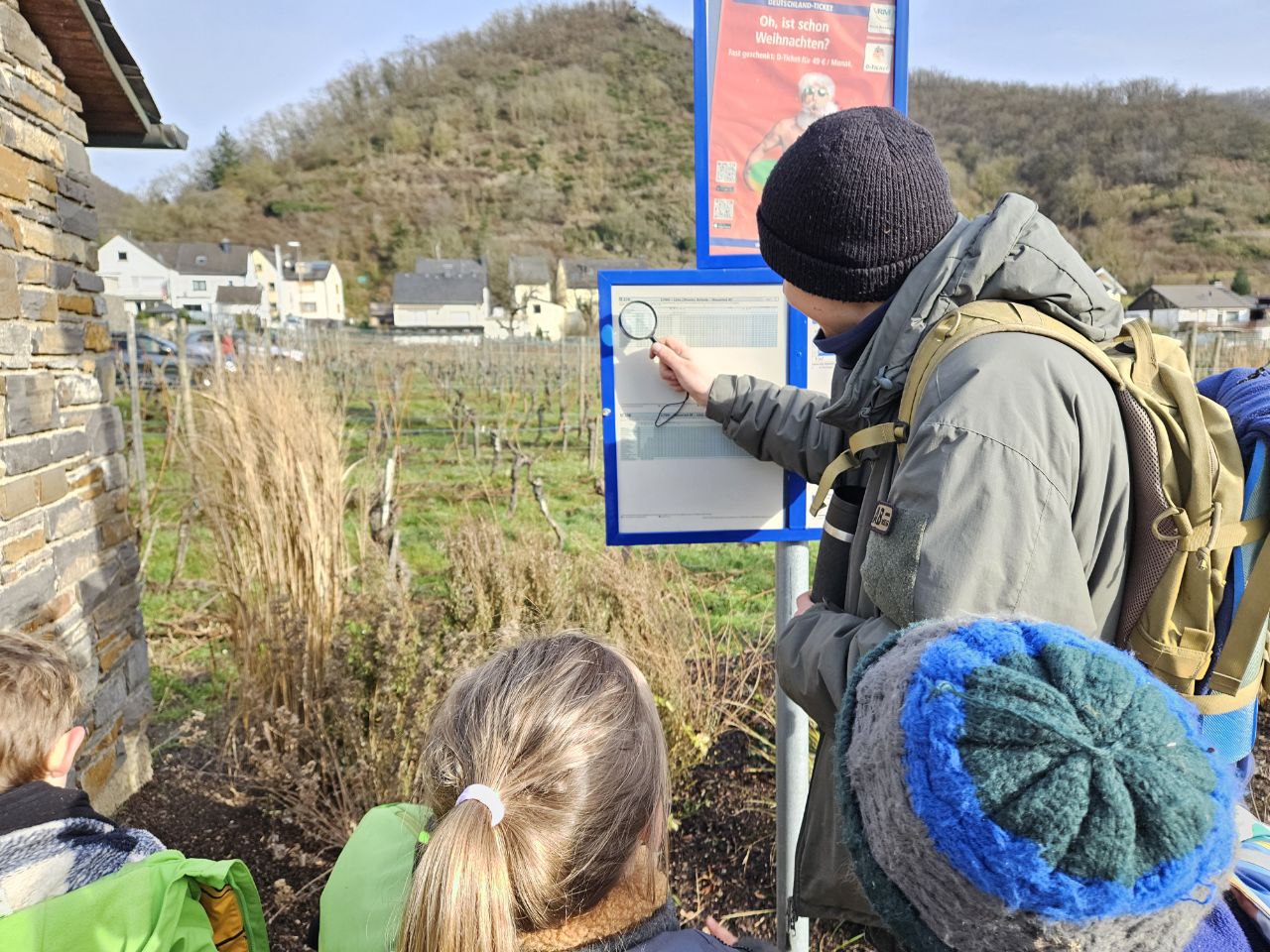 Kinder schauen sich mit einem Erwachsenen den Busfahrplan an.