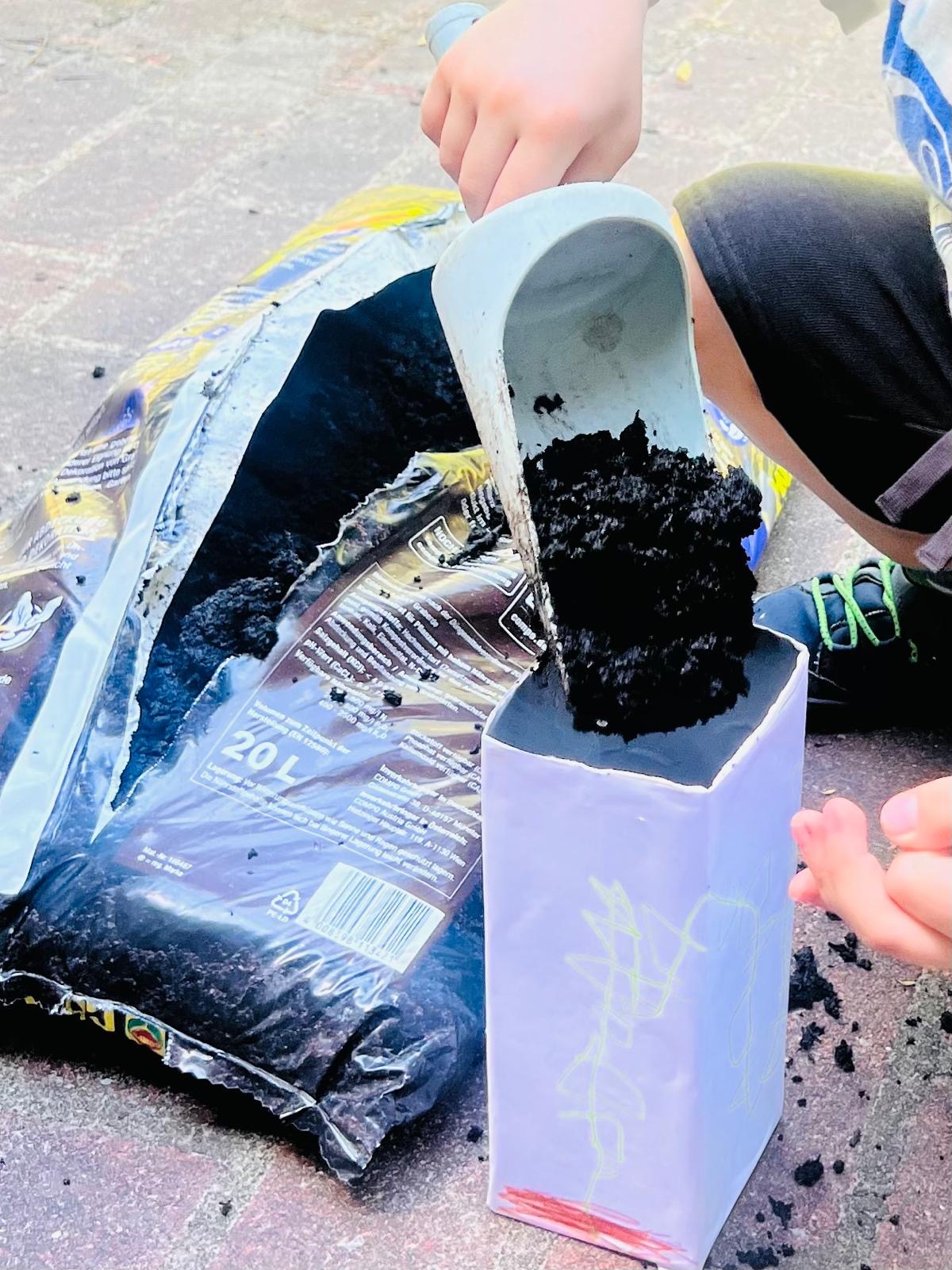 Ein Kind füllt einen Milchkarton mit Erde.