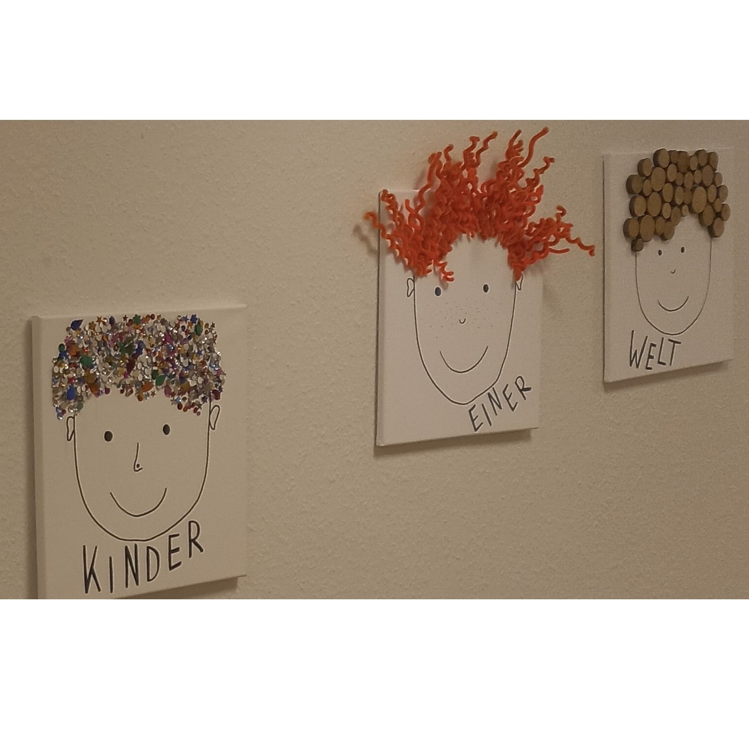 Leinwände mit Kindergesichtern aus unterschiedlichen Materialien, wie Knöpfe