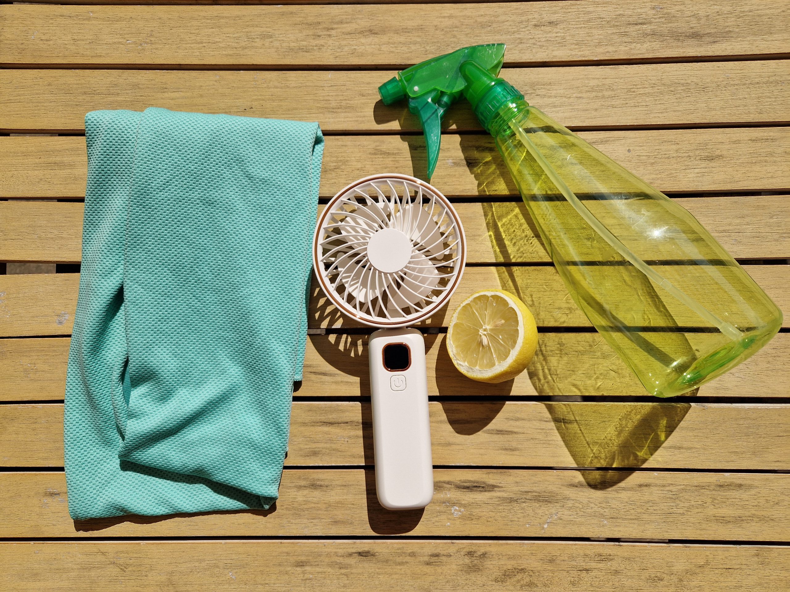 Ein kühlendes Handtuch, ein Handventilator, eine Sprühflasche und eine Zitrone.
