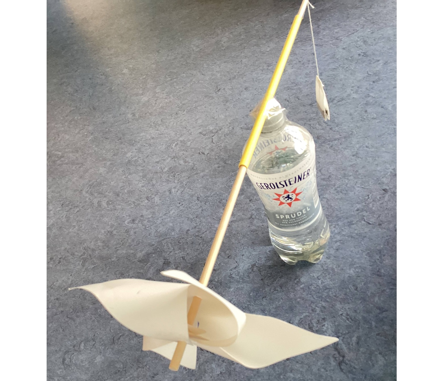 Eine Plastikflasche, auf der ein Windrad mit dem Stab befestigt ist, aam anderen Ende des Stabs hängt ein Teebeutel.